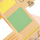 Green square notebook on desk with stationery